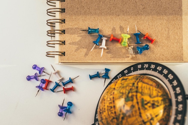 Photo directly above shot of thumbtacks with spiral notebook and globe on gray background