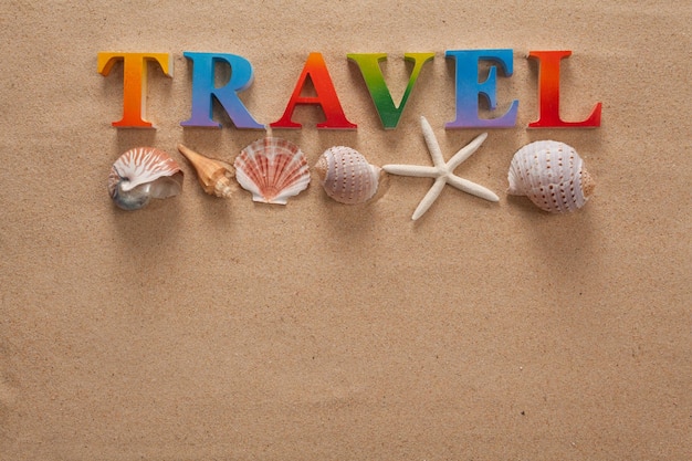 Photo directly above shot of travel text with seashells on sand at beach