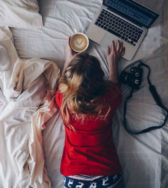 Directly above shot of woman using laptop while lying on bed at home