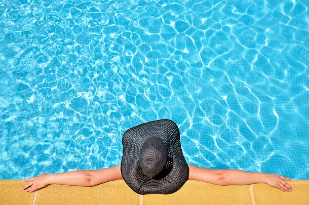 Directly above shot of woman with black hat relaxing in swimming pool