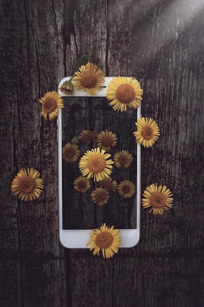 Directly above shot of yellow flowers over smart phone on table