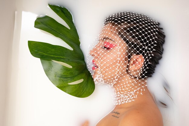 Foto direttamente sopra la foto di una giovane donna con la faccia coperta da una rete che prende un bagno di latte