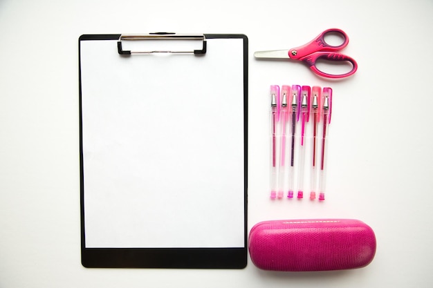 Directly above view of blank clipboard by scissors and pen with case on white background