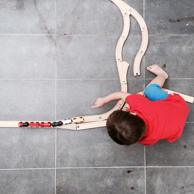 Foto vista direttamente sopra di un ragazzo che gioca con un treno giocattolo sul pavimento