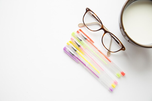 Directly above view of drink by eyeglasses and pens on white table