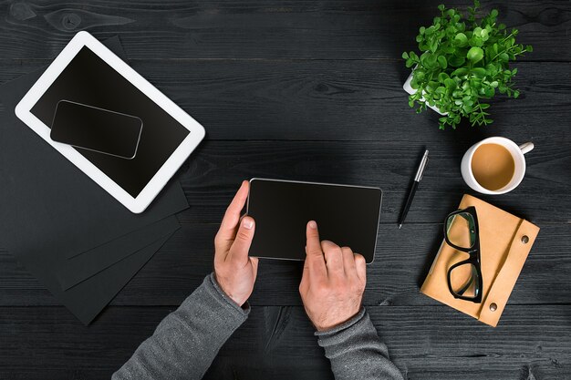 Directly above view of human hands with digital tablet. Digital tablet, diary, coffee cup and potted plant on work desk. Man working from home.