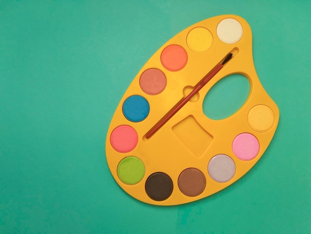 Photo directly above view of palette and paintbrush on colored background