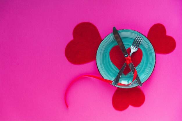 Photo directly above view of plate and cutlery with heart shape against pink background