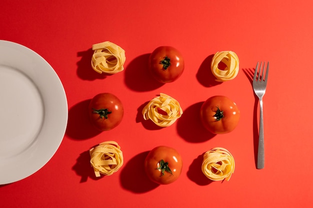 Photo directly above view of ribbon pasta with tomatoes amidst plate and fork on red background. unaltered, organic food and healthy eating concept.