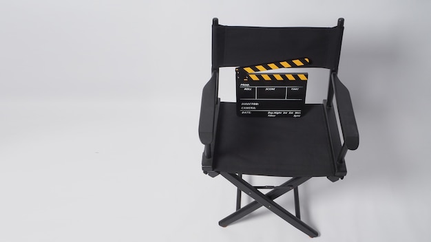 Foto sedia regista con ciak nero e giallo o ardesia cinematografica su sfondo bianco.it è utilizzato nella produzione video e nell'industria cinematografica.