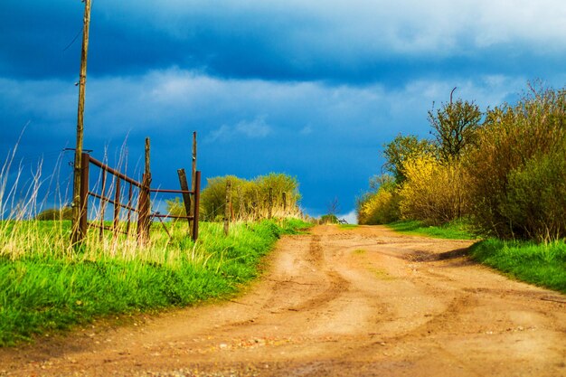 Dirt road amidst field against sky