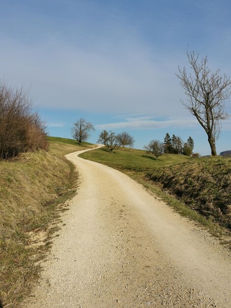 Dirt road amidst field against sky