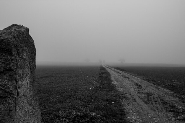 Photo dirt road on field against sky during foggy weather