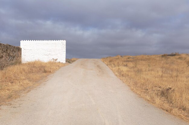 Dirt road between field and white house Horizontal