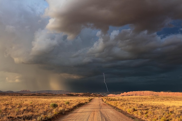 Photo a dirt road leading to dark ominous storm clouds and lightning in southern utah