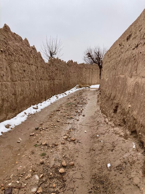 Photo a dirt road leads through a wall with a snow covered ground.