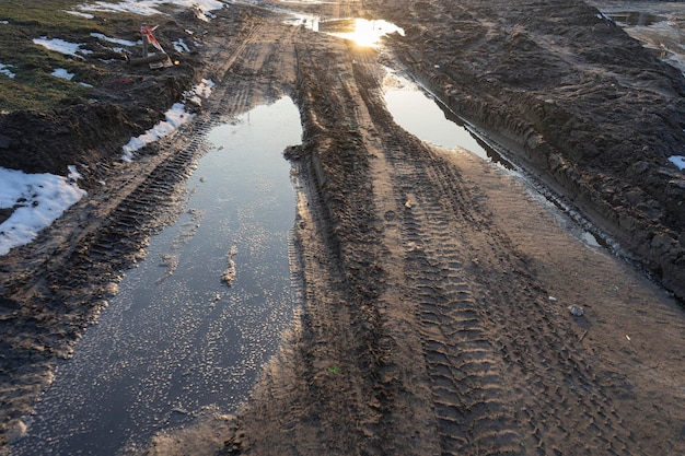 日没に対する雨の後の春の草原の未舗装の道路