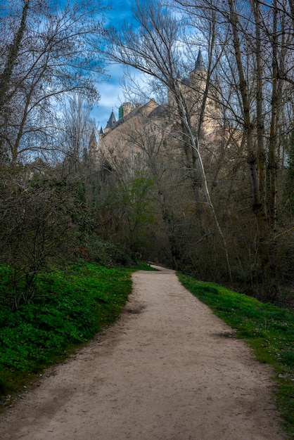 Dirt road between trees and grass in the direction of the Alcazar of Segovia on a winter day with beautiful clouds and green grass on the ground