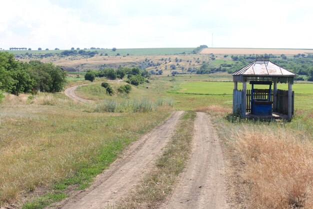 A dirt road with a gazebo in the middle of a field