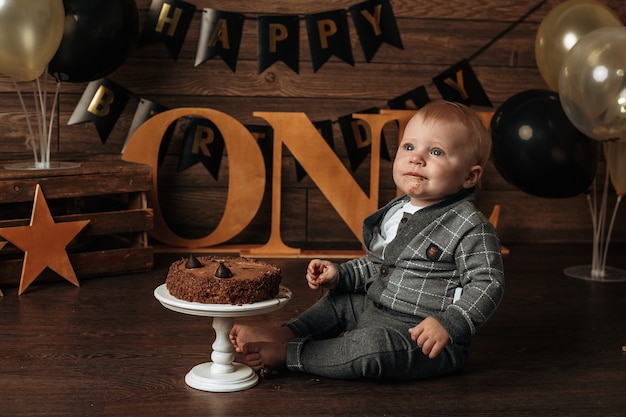A dirty birthday boy in a gray suit eats a chocolate cake on a brown background