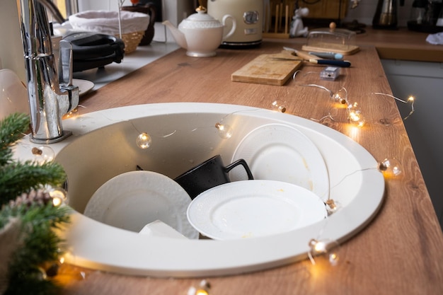 Dirty dishes in the sink in the garlanded kitchen a holiday after a feast at Christmas Mess after the guests for the New Year kitchen cleaning detergent cleaning services