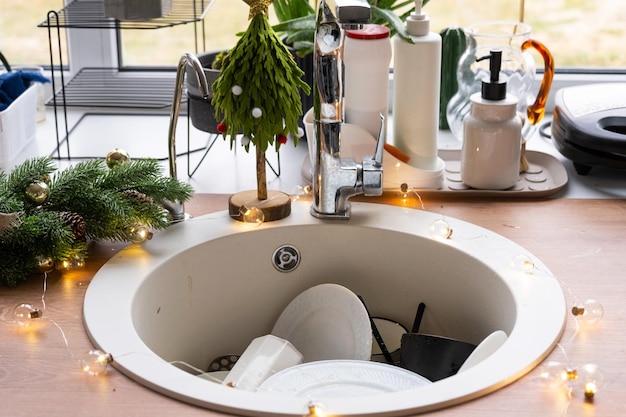 Dirty dishes in the sink in the garlanded kitchen a holiday after a feast at Christmas Mess after the guests for the New Year kitchen cleaning detergent cleaning services