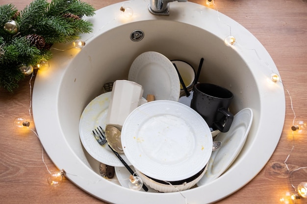 Dirty dishes in the sink in the garlanded kitchen a holiday\
after a feast at christmas mess after the guests for the new year\
kitchen cleaning detergent cleaning services