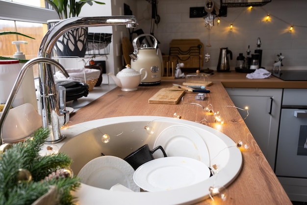 Dirty dishes in the sink in the garlanded kitchen a holiday
after a feast at christmas mess after the guests for the new year
kitchen cleaning detergent cleaning services