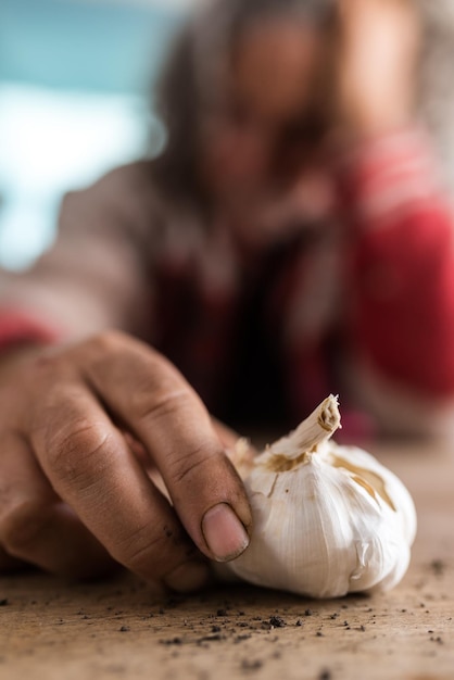 Foto mano sporca di un uomo coperto di terra con un bulbo d'aglio fresco e terra sparsa su un tavolo di legno rustico in una vista ravvicinata