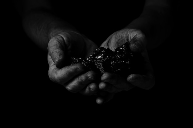 Dirty hands miner holding coal in black and white photoHeavy coal mining