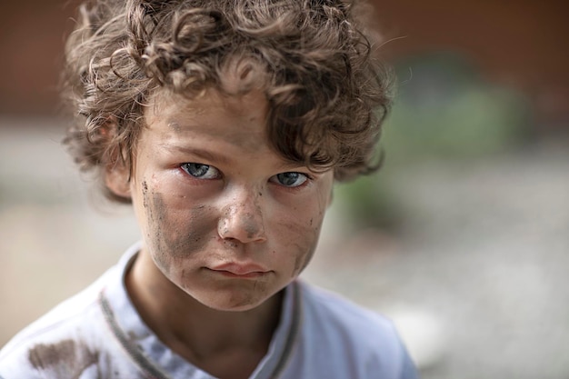 Dirty homeless boy looks through eyes full of tears