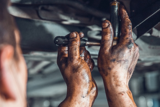 トルクレンチで汚れた男性の手。ワークショップで車を修理する技術者