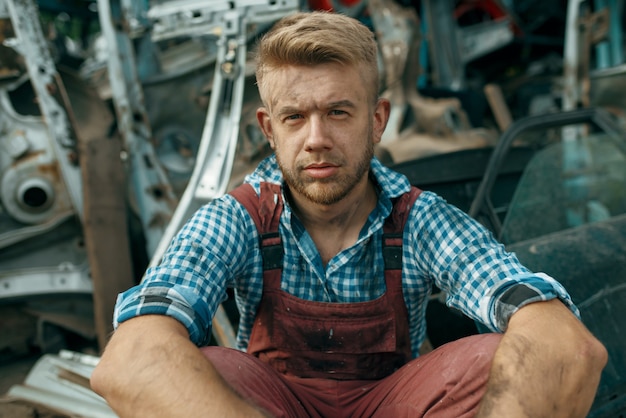 Dirty male repairman with wrench on car junkyard