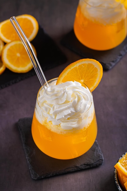 Dirty orange soda with whipped cream in glasses and orange slices on the table vertical view