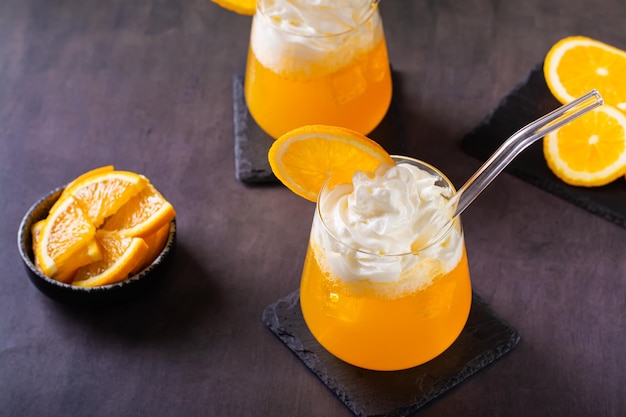 Dirty orange soda with whipped cream in glasses and orange slices on the table