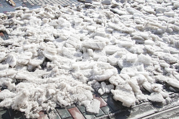 Dirty pieces of ice melting under spring sun on side of road after cleaning the sidewalk