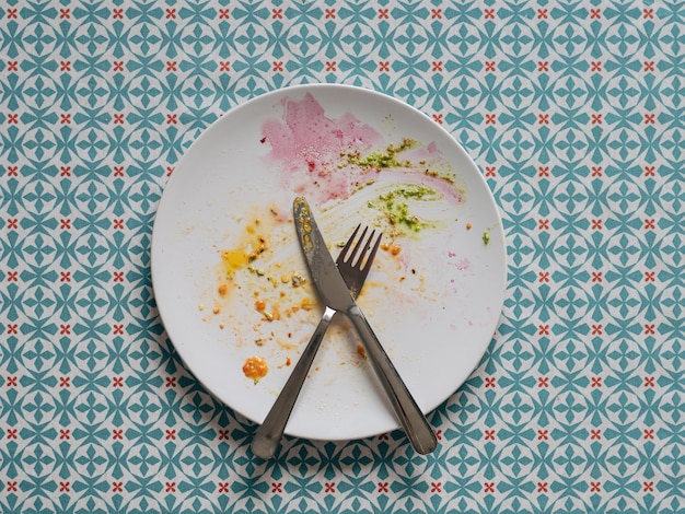 Dirty plate after healthy vegetarian paleo lunch white plate and colorful dirty after egg yolk beet and green pesto over blue tablecloth top view or flat lay