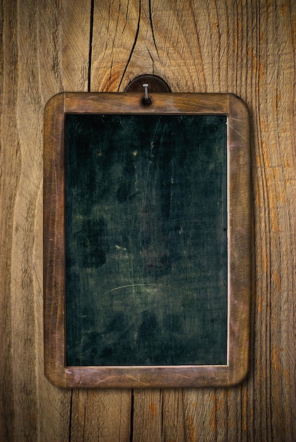 Dirty and scratched wooden school slate over a wood wall, vertical image