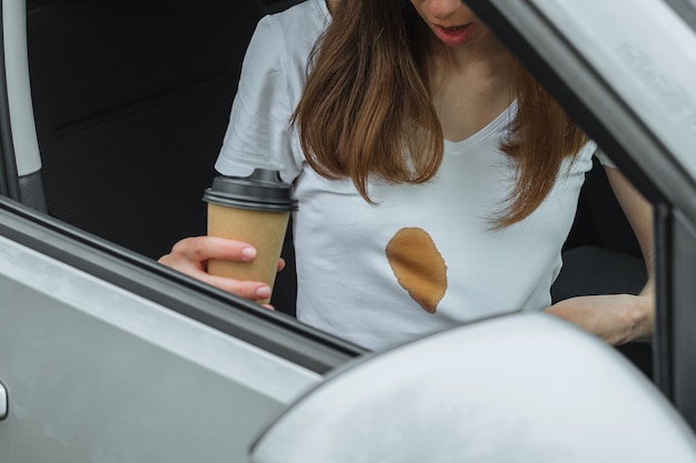 白い服に染みを見せている女性を運転中にこぼれたコーヒーの汚れた染み