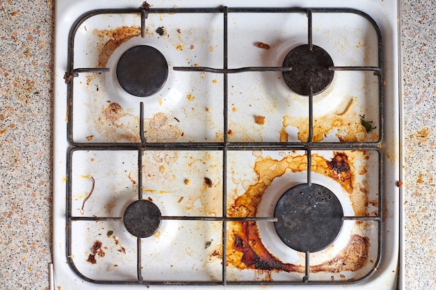 Photo dirty stove with food leftovers. unclean gas kitchen cooktop with greasy spots, old fat stains, fry spots and oil splatters.