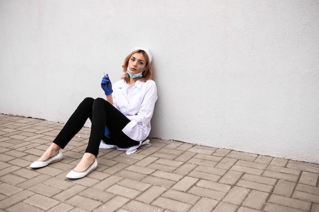 Dirty tired nurse with ash on face sitting outside hospital and\
smoking