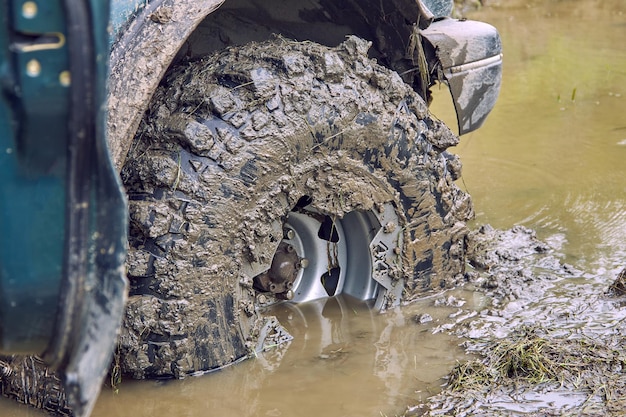 The dirty wheel of a 4x4 offroad car is half drowned in a puddle