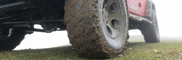 Dirty wheel with rubber tire of large car parked on green grass under cloudy sky powerful