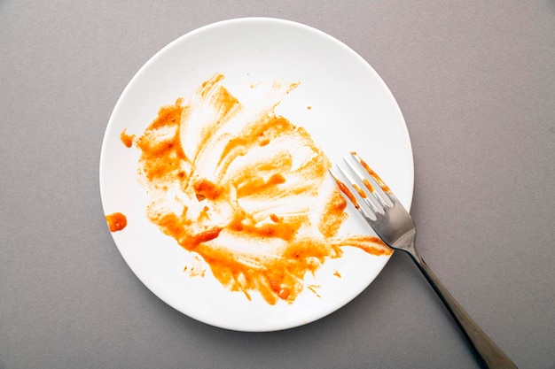 Dirty white ceramic plate with tomato sauce stains food leftovers and fork top view