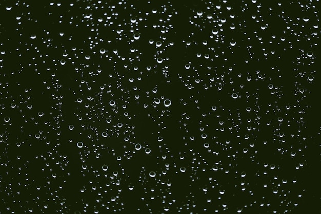 Dirty window glass with drops of rain. Atmospheric green background with raindrops. Droplets and stains close up. Detailed transparent texture in macro with copy space. Rainy weather.