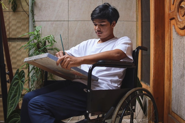 Disabled Asian man on wheelchair painting on canvas at home