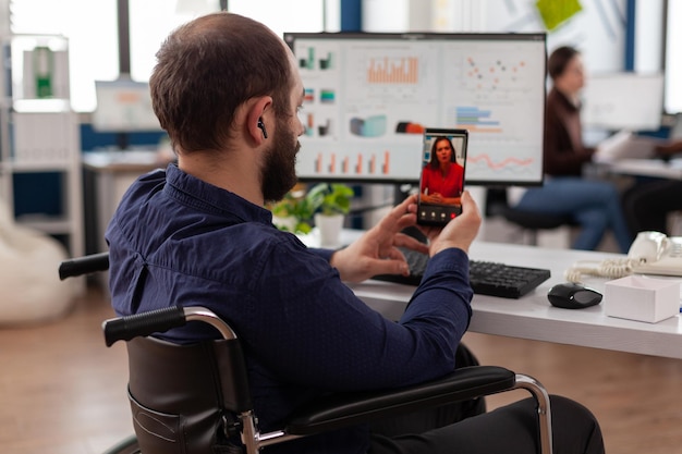 Disabled businessman holding smartphone talking with remote manager during online videocall meeting conference working in startup business office. Teleconference call on phone screen