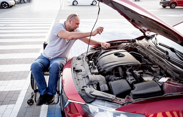 L'uomo disabile in sedia a rotelle controlla il motore della sua auto al parcheggio