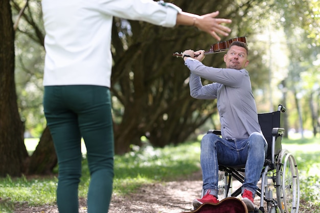 Disabled man in wheelchair is swinging violin at woman in park earning opportunities for people