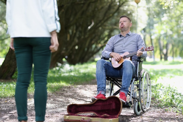 L'uomo disabile in sedia a rotelle scherza con la donna mentre suona l'ukulele nel concetto di parco di